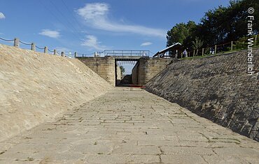 Ein Flussbett aus Steinen gebaut, am Ende eine Brücke mit Schleusentoren