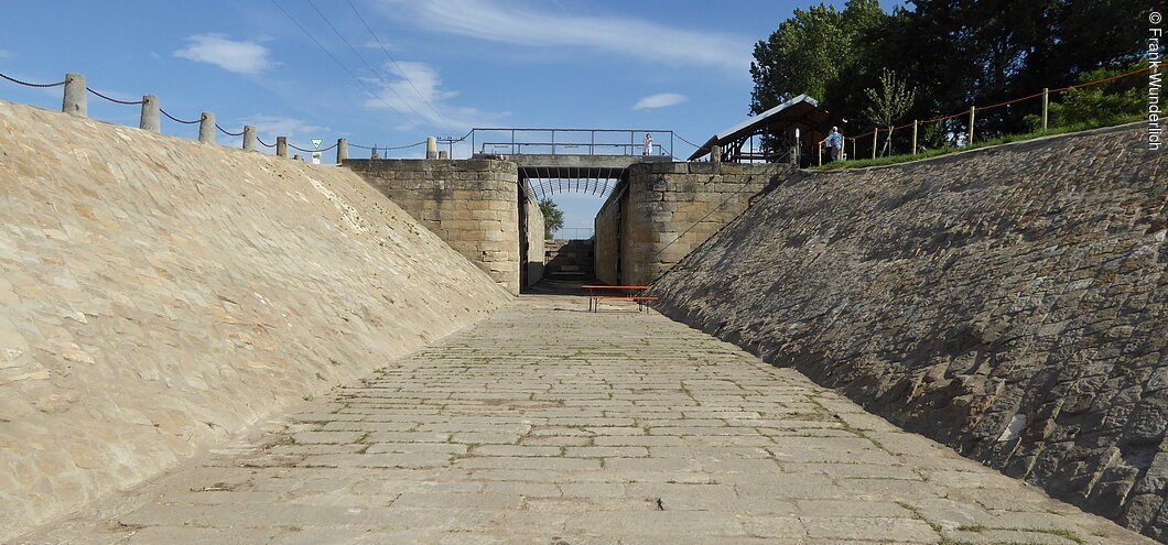 Ein Flussbett aus Steinen gebaut, am Ende eine Brücke mit Schleusentoren