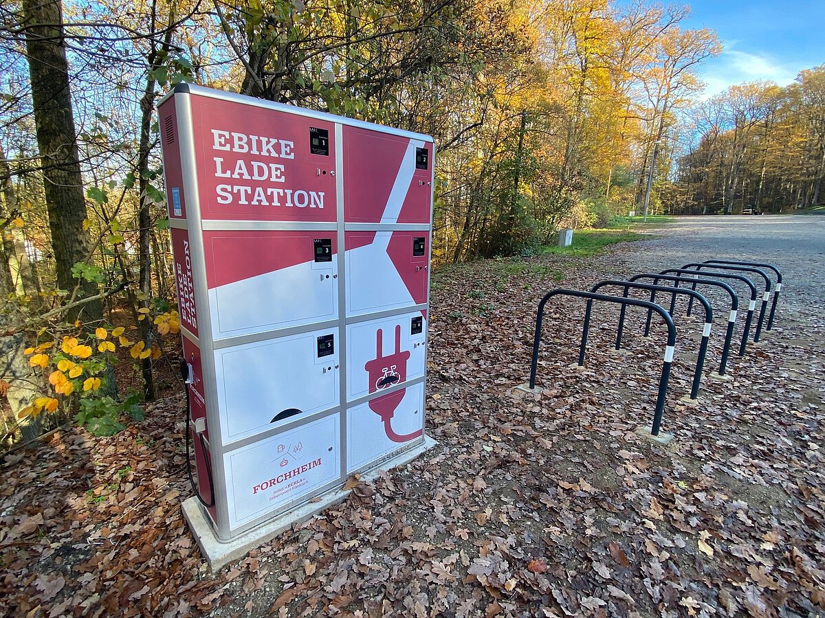 Eine rot-weiße E-Bike-Ladestation, davor mehrere Fahrradständer