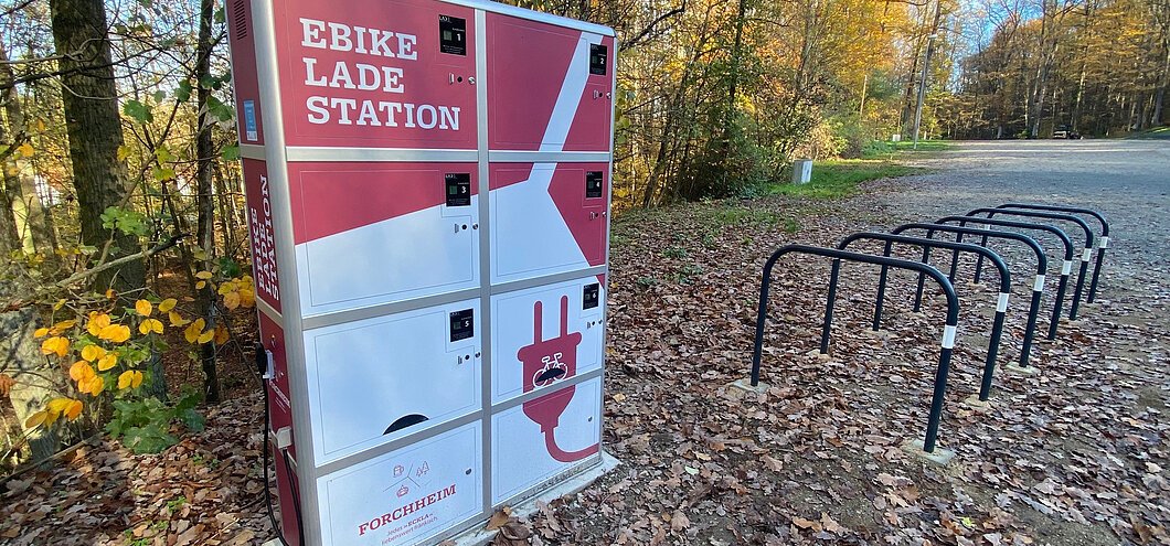 Eine rot-weiße E-Bike-Ladestation, davor mehrere Fahrradständer