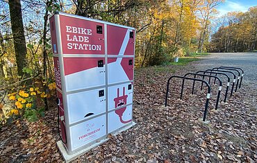 Eine rot-weiße E-Bike-Ladestation, davor mehrere Fahrradständer