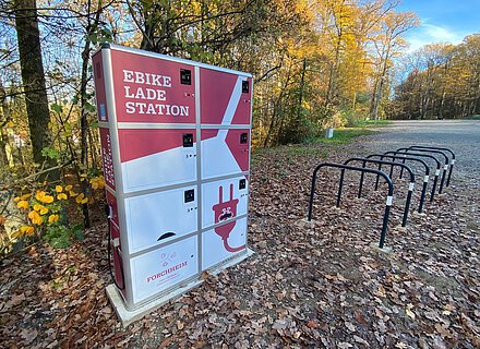 Eine rot-weiße E-Bike-Ladestation, davor mehrere Fahrradständer