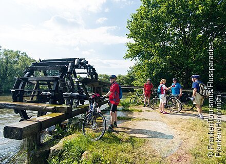 Personen mit Fahrrad an einem großen Wasserrad