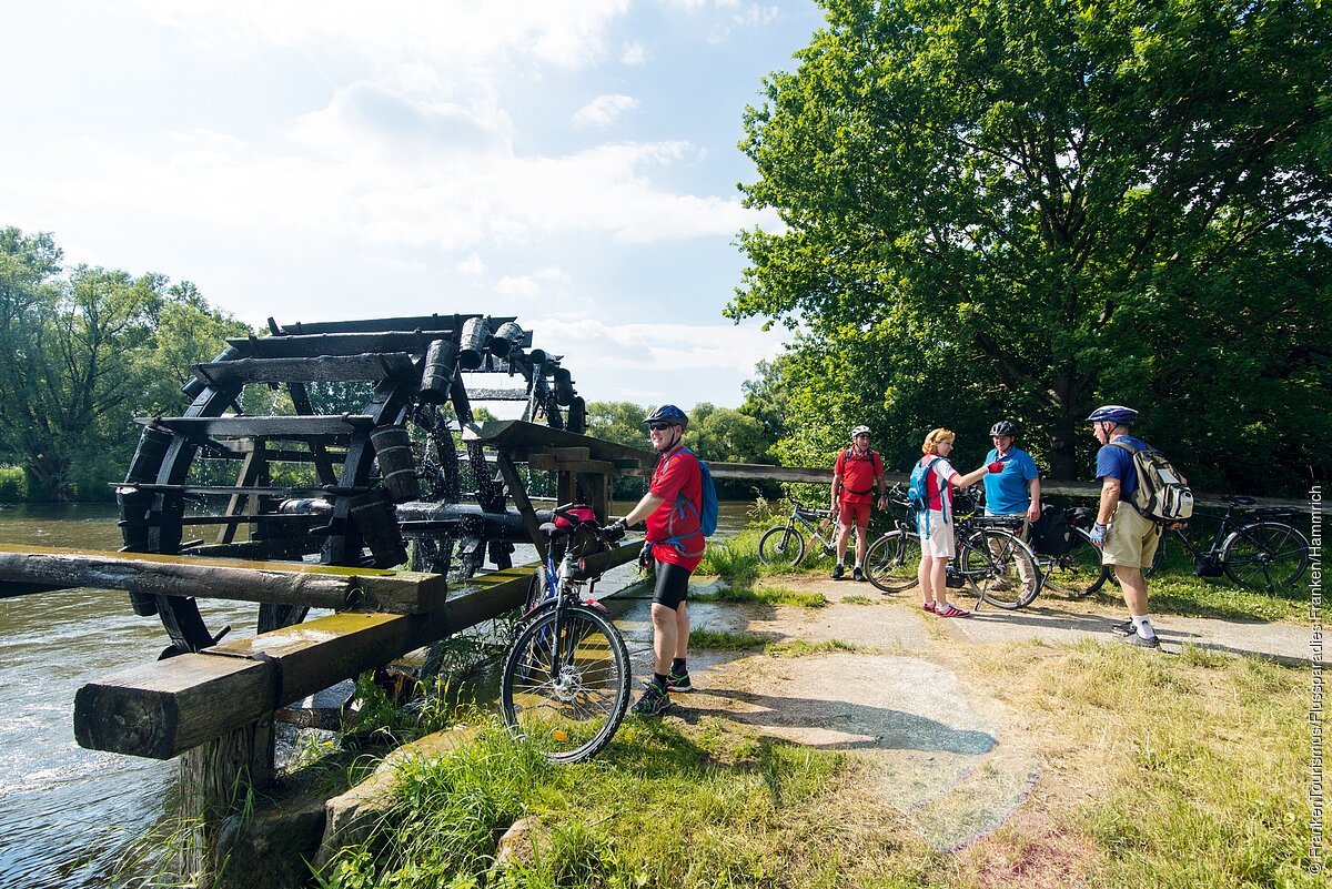Personen mit Fahrrad an einem großen Wasserrad