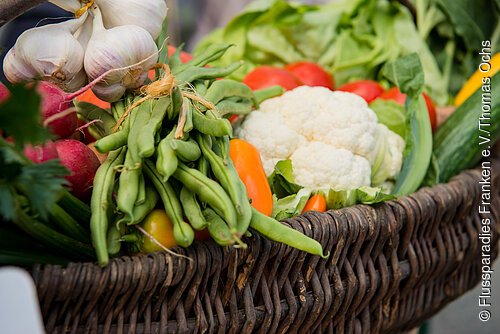 Nahaufnahme eines Korbs mit grünem Gemüse, Blumenkohl, Knoblauch und roten Radieschen.